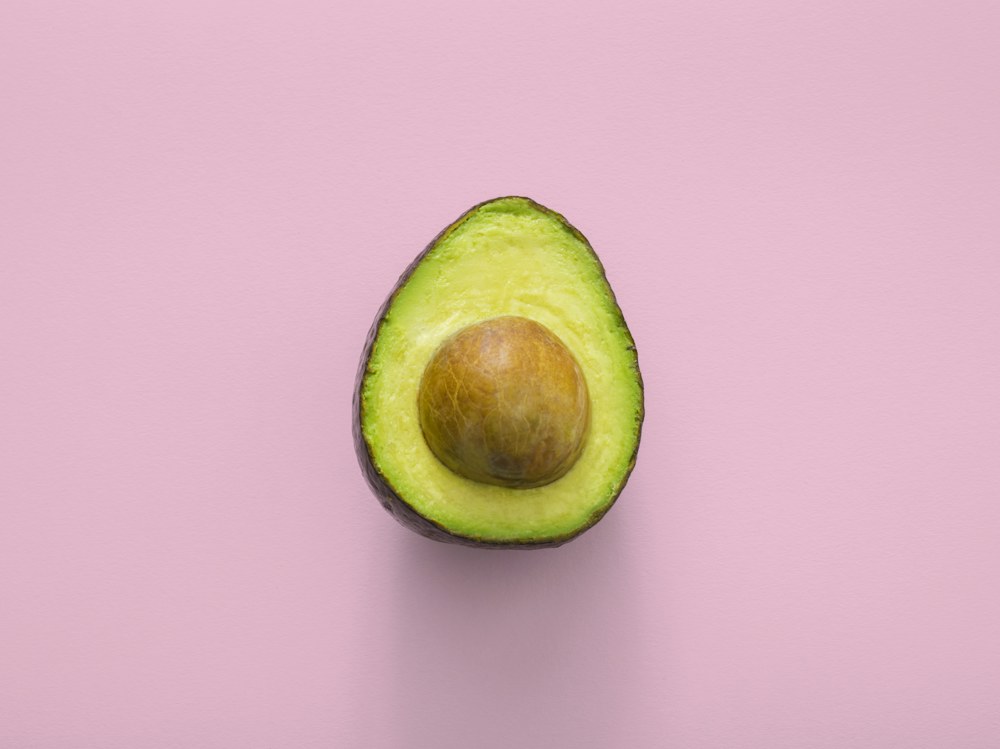 An avocado half with its stone on a pink background, original photo