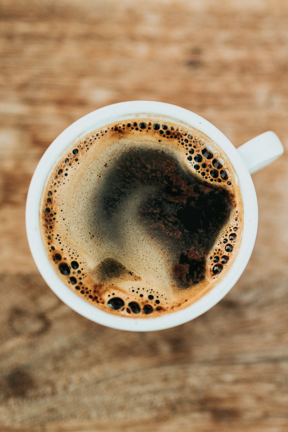 An overhead view of a cup of black coffee on a wooden table, original photo
