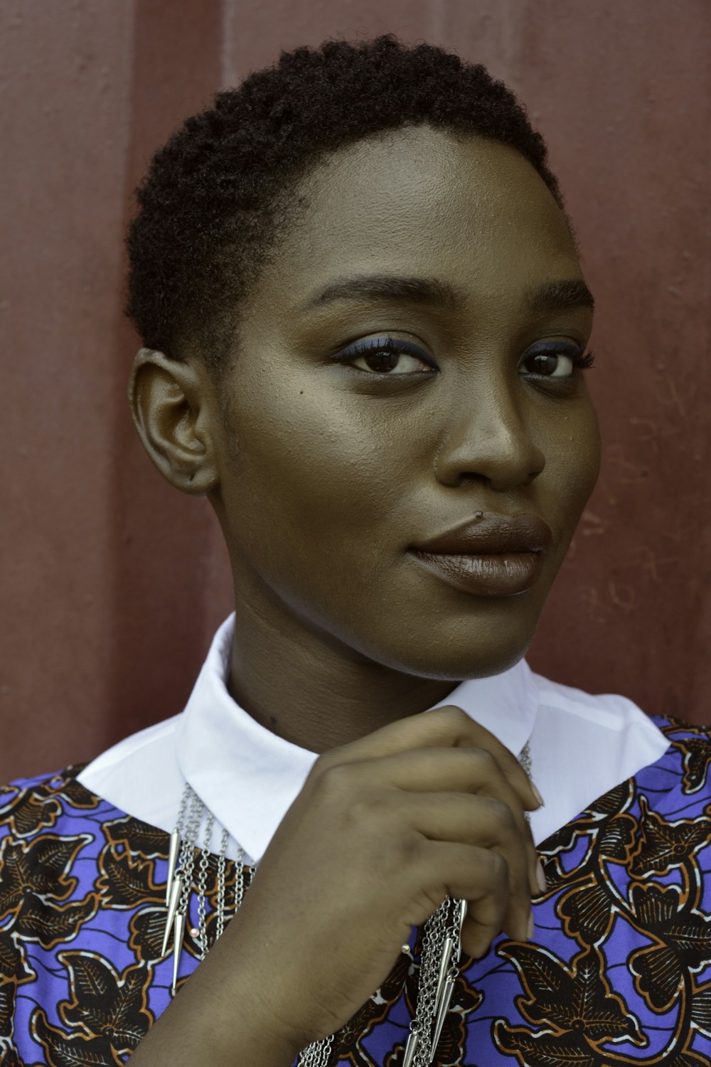A woman with short natural hair and a patterned top resting her hand under her chin, original photo