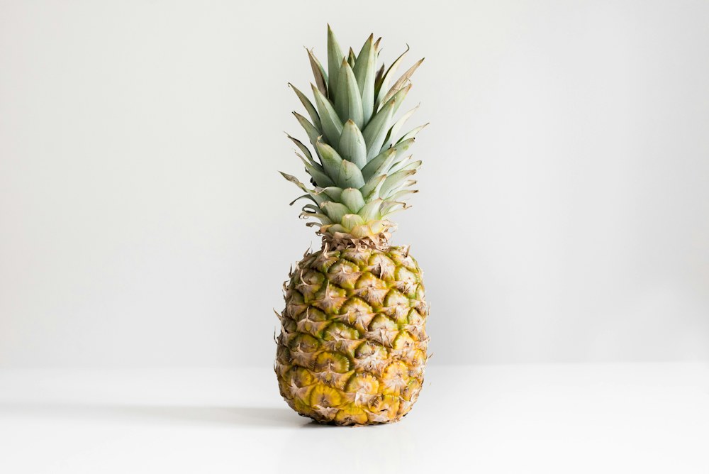 A whole pineapple with spiky green leaves on a light studio background, original photo