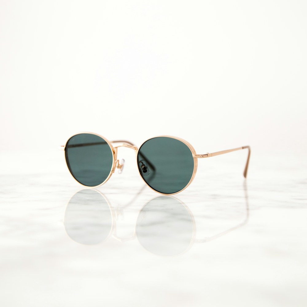 Round green-lens sunglasses with a fine gold frame on a white surface, original photo
